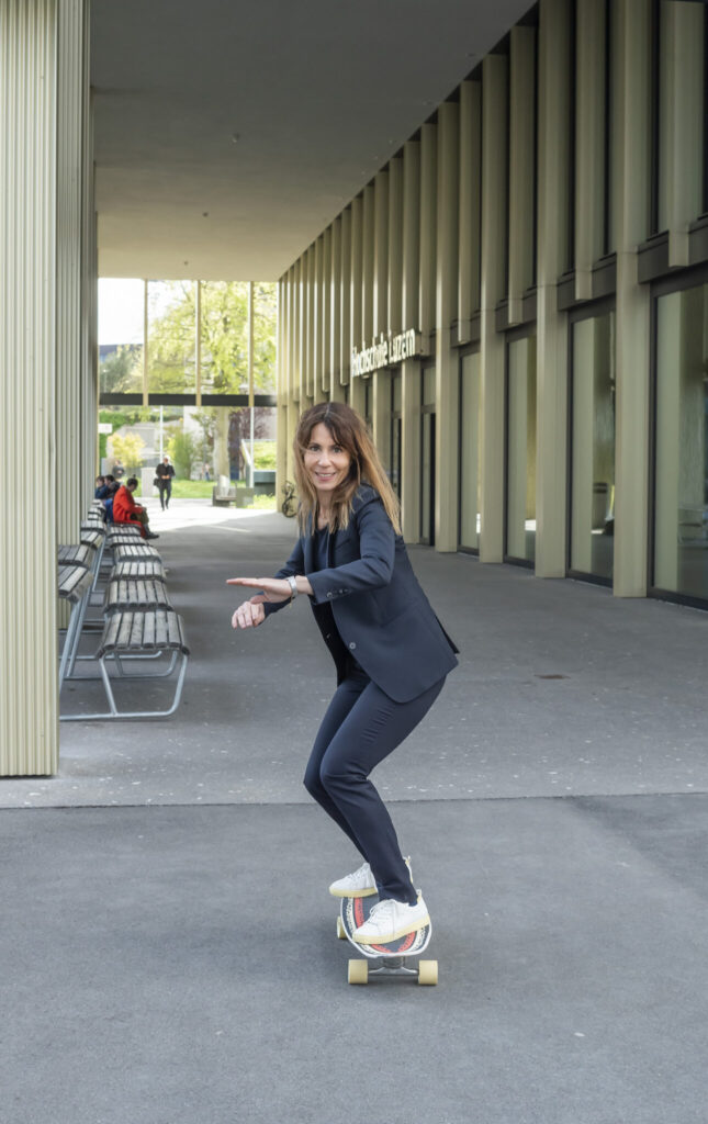 Bild von Sarah Hauser auf Skateboard vor dem Gebäude der HSLU in Rotkreuz