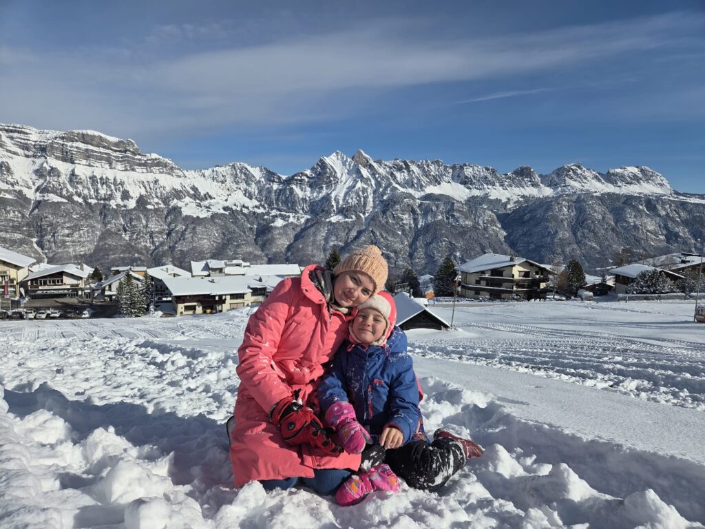 Aygul und ihre Tochter sitzen im Schnee. im Hintergrund die Kulisse der Flumerberge.