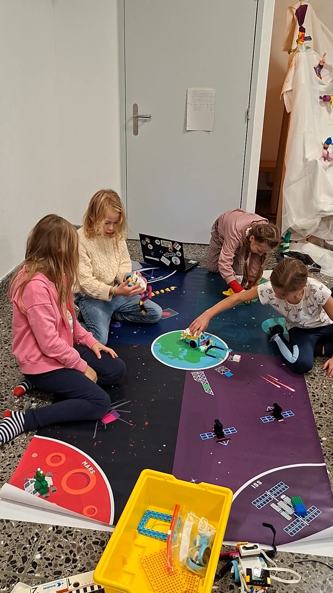 Kinder sitzen am Boden und bedienen Lego-Roboter