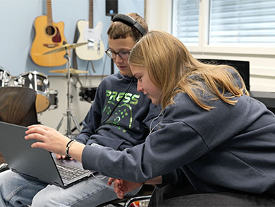 Zwei Jugendliche in einem Musikunterrichtszimmer schauen auf einen Laptop. Bild: HSLU